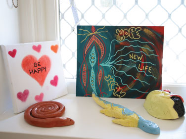 A windowsill with art placed on it. There is a canvas with a love heart and the words "BE HAPPY", alongside a terracotta coloured ceramic snake and a blue/yellow lizard.