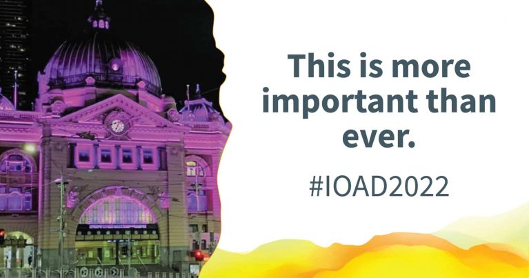 Flinders Street Station lit up with purple light. Text alongside reads: "This is more important than ever. #IOAD2022"