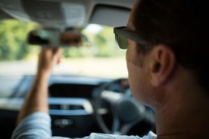 Person in driver seat of car looking in rear-view mirror