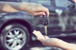Image of a person passing car keys to another person, with a car in the background